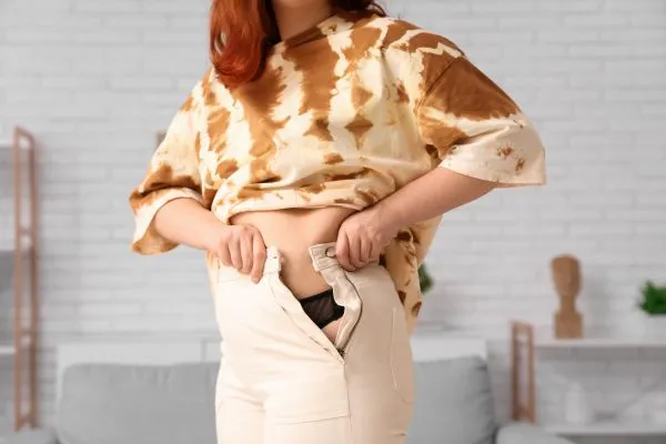 Image of woman trying to do her trousers up after pregnancy weight gain Sleaford